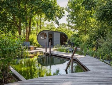 Ein Schwimmteich im kleinen Garten mit einem Sauna Haus umringt von Bäumen